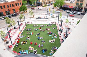 A large group of people are sitting on a grassy area in the middle of a city square